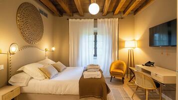 A hotel room with a large bed, a desk, a chair, a TV, and a lamp.