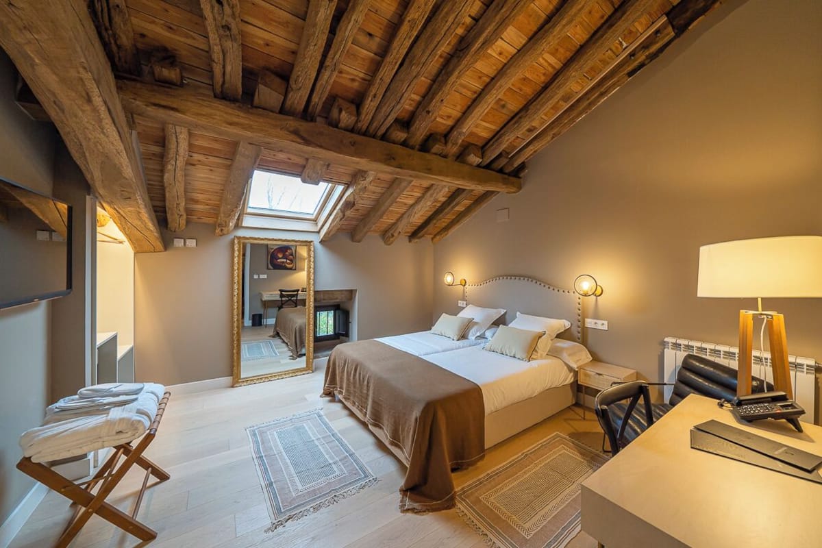 Une chambre avec un plafond en pente, un grand lit, des lampes de chevet, un bureau et un miroir.