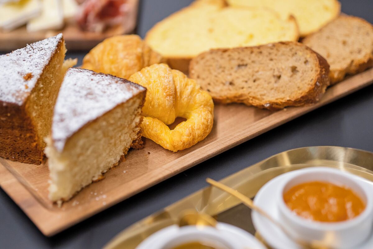 A wooden board with a slice of cake, a croissant, and slices of bread.