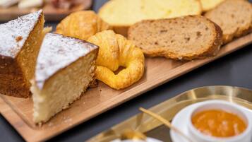 A wooden board with a slice of cake, a croissant, and slices of bread.