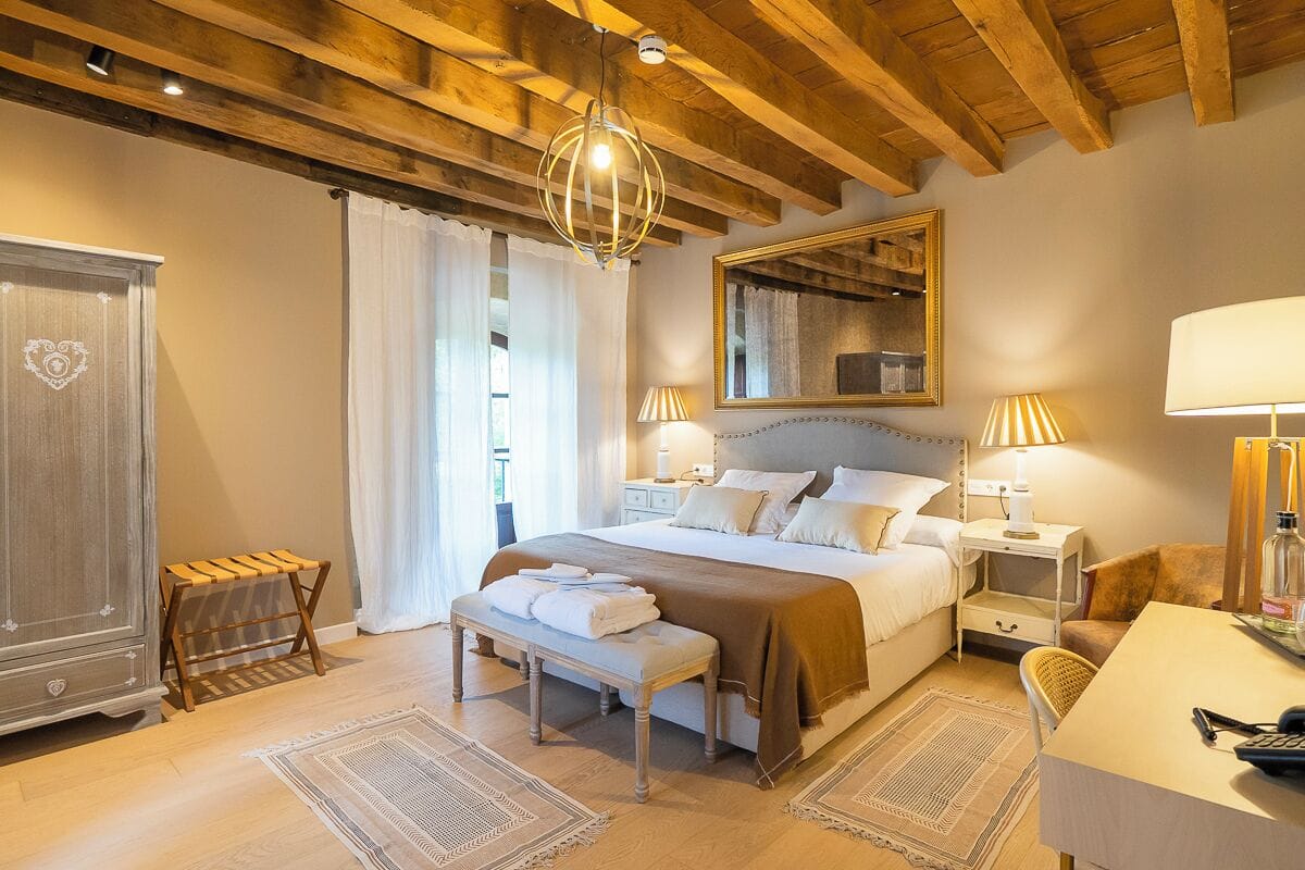 Une chambre à coucher avec un grand lit, des lampes de chevet, une armoire en bois, un banc et un bureau avec une chaise.