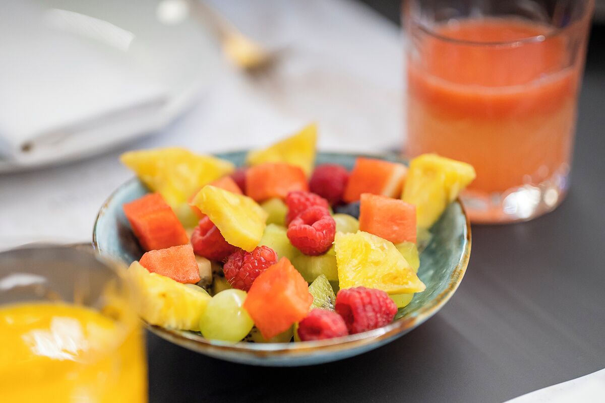 A bowl of mixed fruit salad with a glass of orange juice in the background.