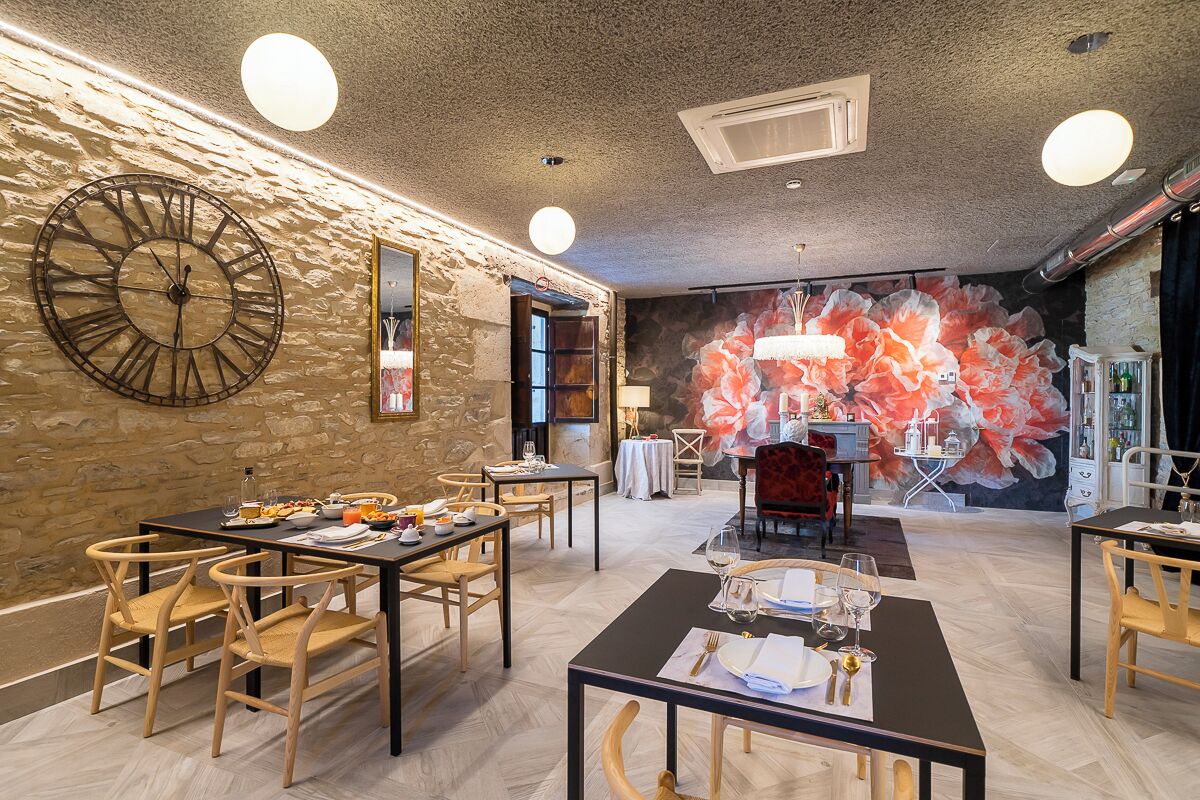 Un comedor con sillas y mesas de madera, un reloj grande en la pared y un mural floral al fondo.