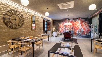 Un comedor con sillas y mesas de madera, un reloj grande en la pared y un mural floral al fondo.