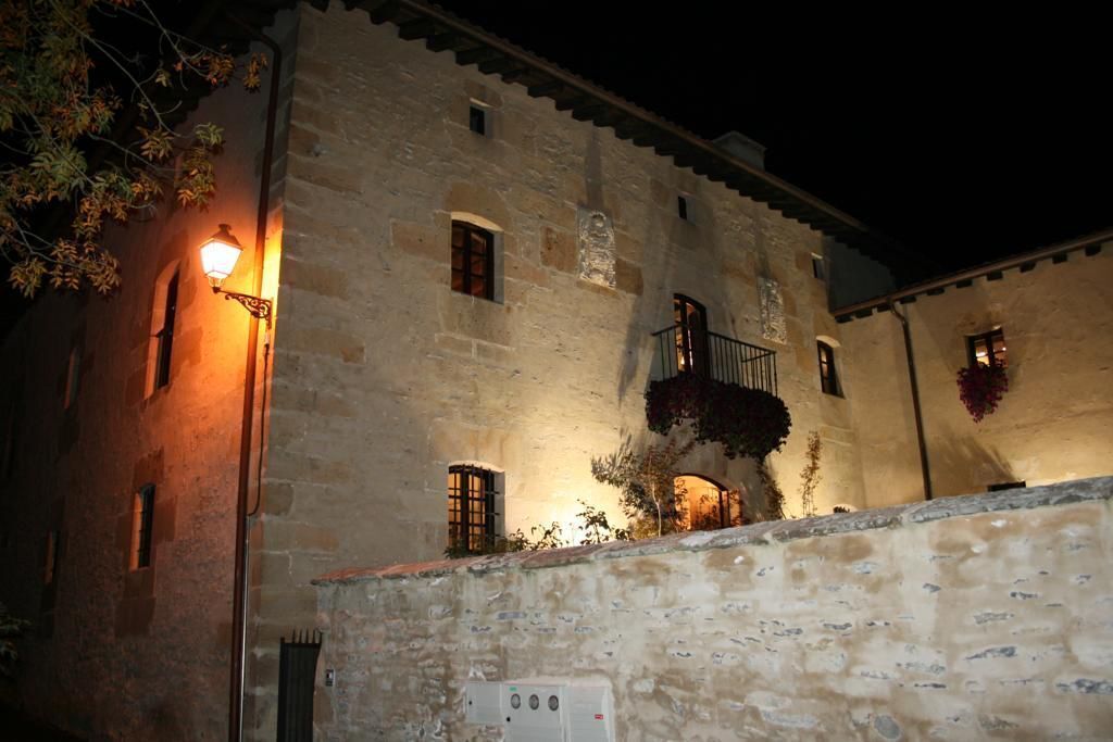 A stone building with a balcony, a lit lamp, and a wall-mounted electrical box.