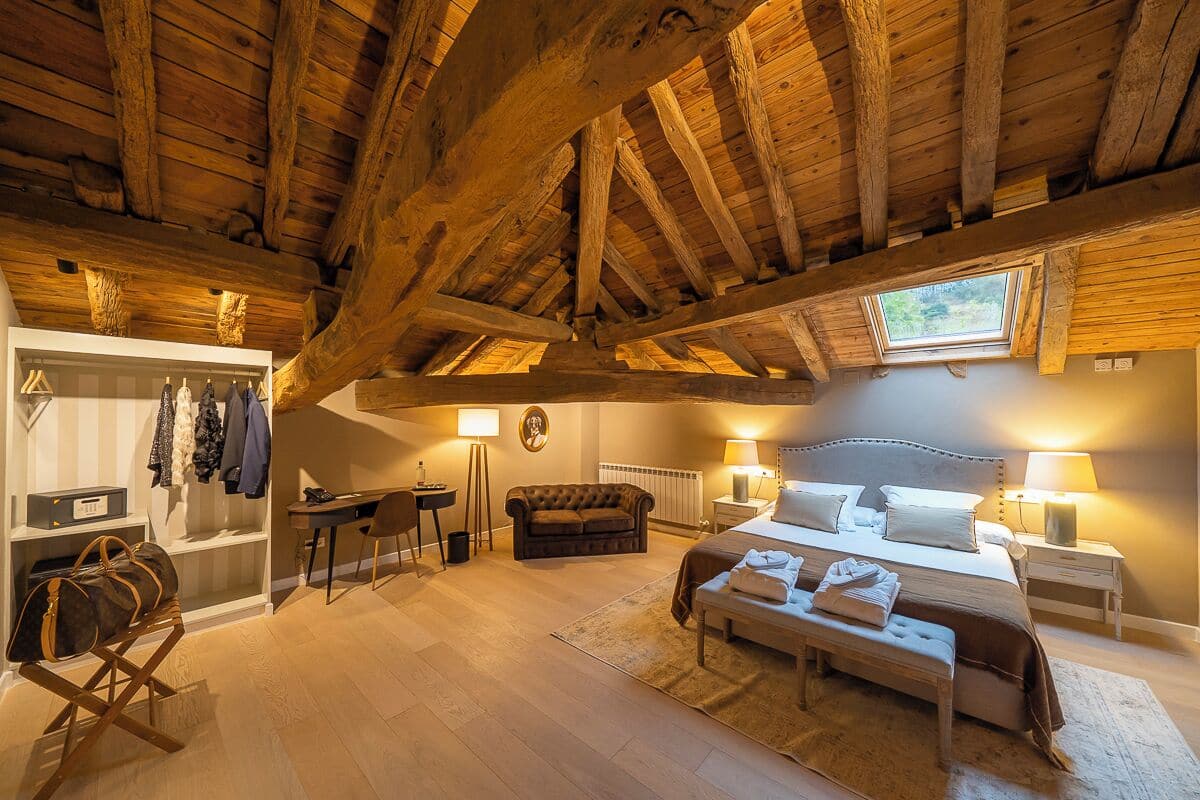 Une chambre à coucher avec un plafond en bois, un lit, des lampes de chevet, un banc, un bureau et une chaise.