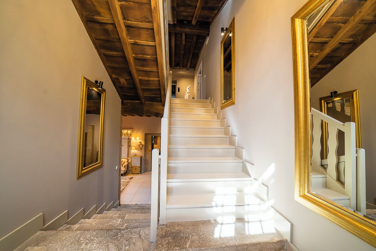 A staircase with white steps leading to a second floor, flanked by walls with large golden-framed mirrors.