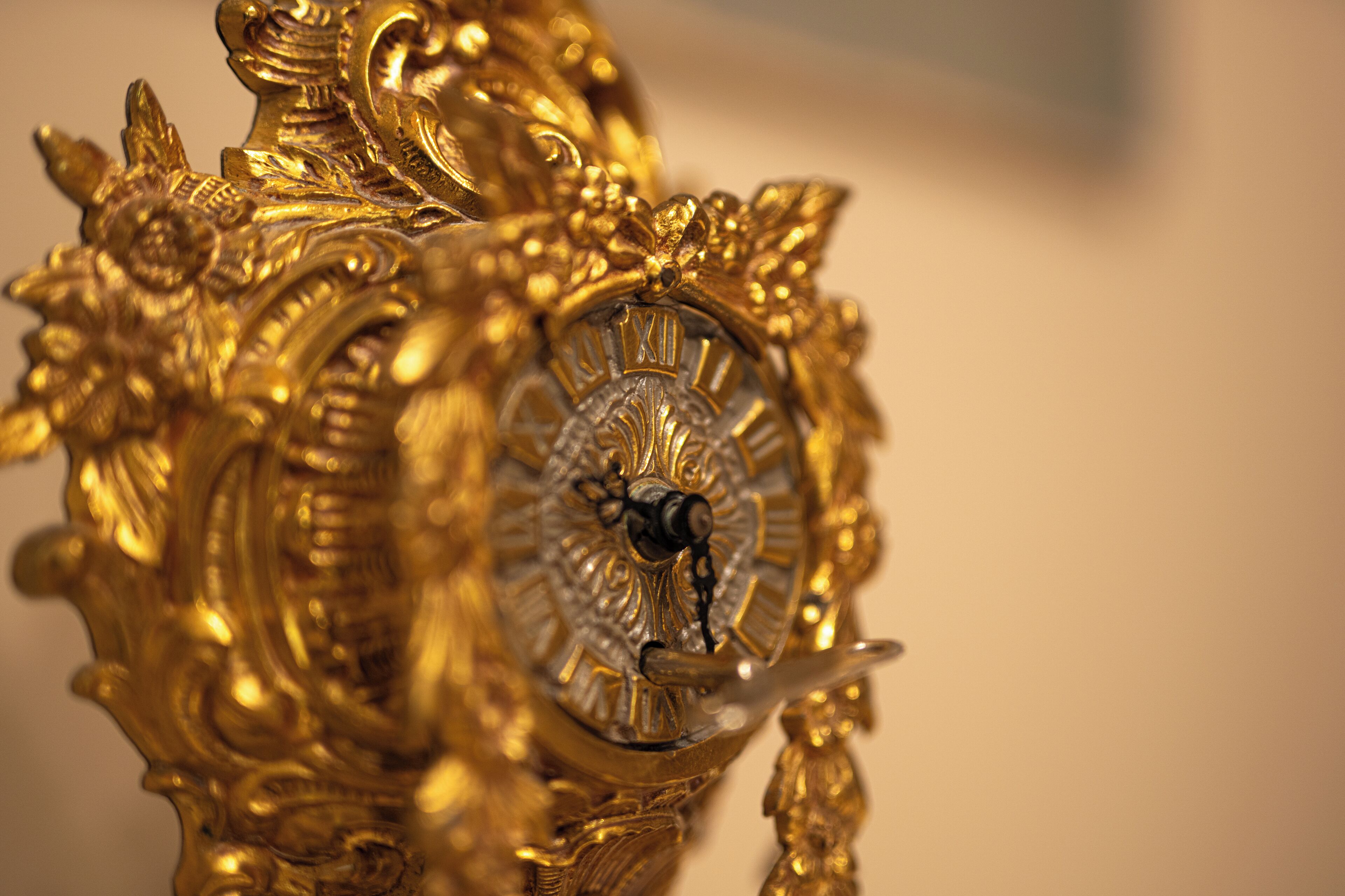 Un primer plano de un reloj dorado ornamentado con detalles intrincados y esfera con números romanos.