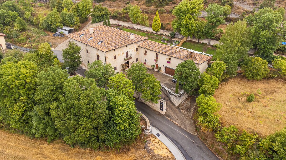 Um edifício de dois andares com telhado de telhas, cercado por vegetação densa e uma estrada sinuosa.
