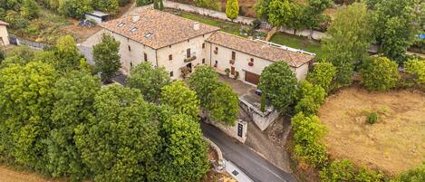 Um edifício de dois andares com telhado de telhas, cercado por vegetação densa e uma estrada sinuosa.