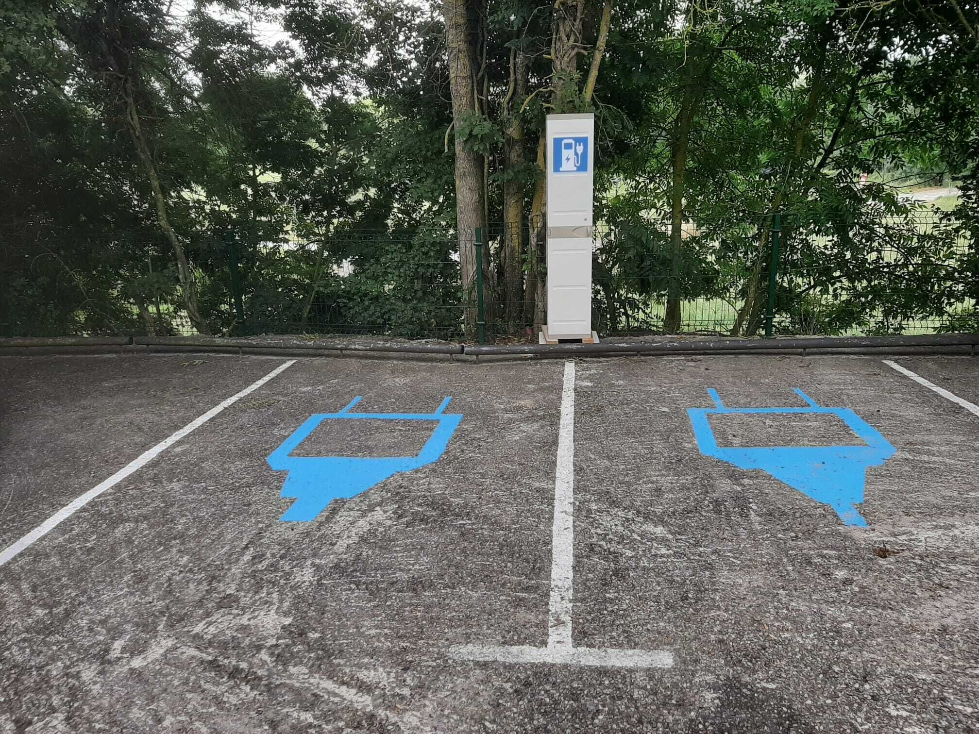 Un espace de stationnement comprenant deux places de stationnement bleues réservées aux personnes handicapées et un panneau indiquant la présence d’une borne de recharge.