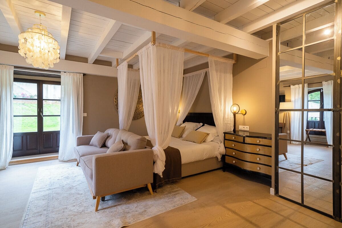 Une chambre à coucher avec un lit à baldaquin, un canapé, une commode et une grande fenêtre avec des rideaux.