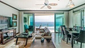 Una sala de estar moderna con un gran ventanal, un ventilador de techo y un comedor con vistas al océano.