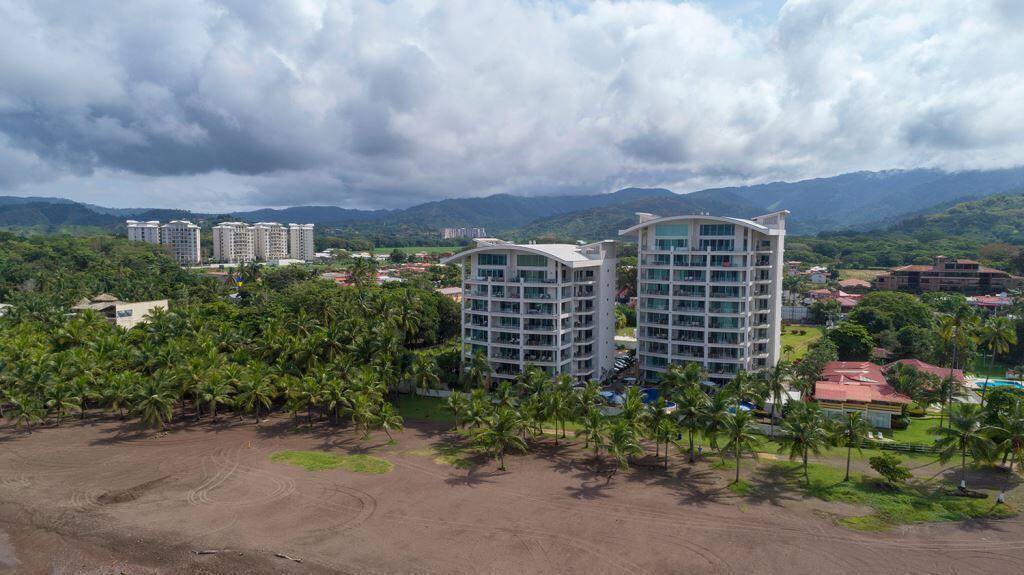 Un hotel moderno con diversi piani, immerso nel verde e palme.