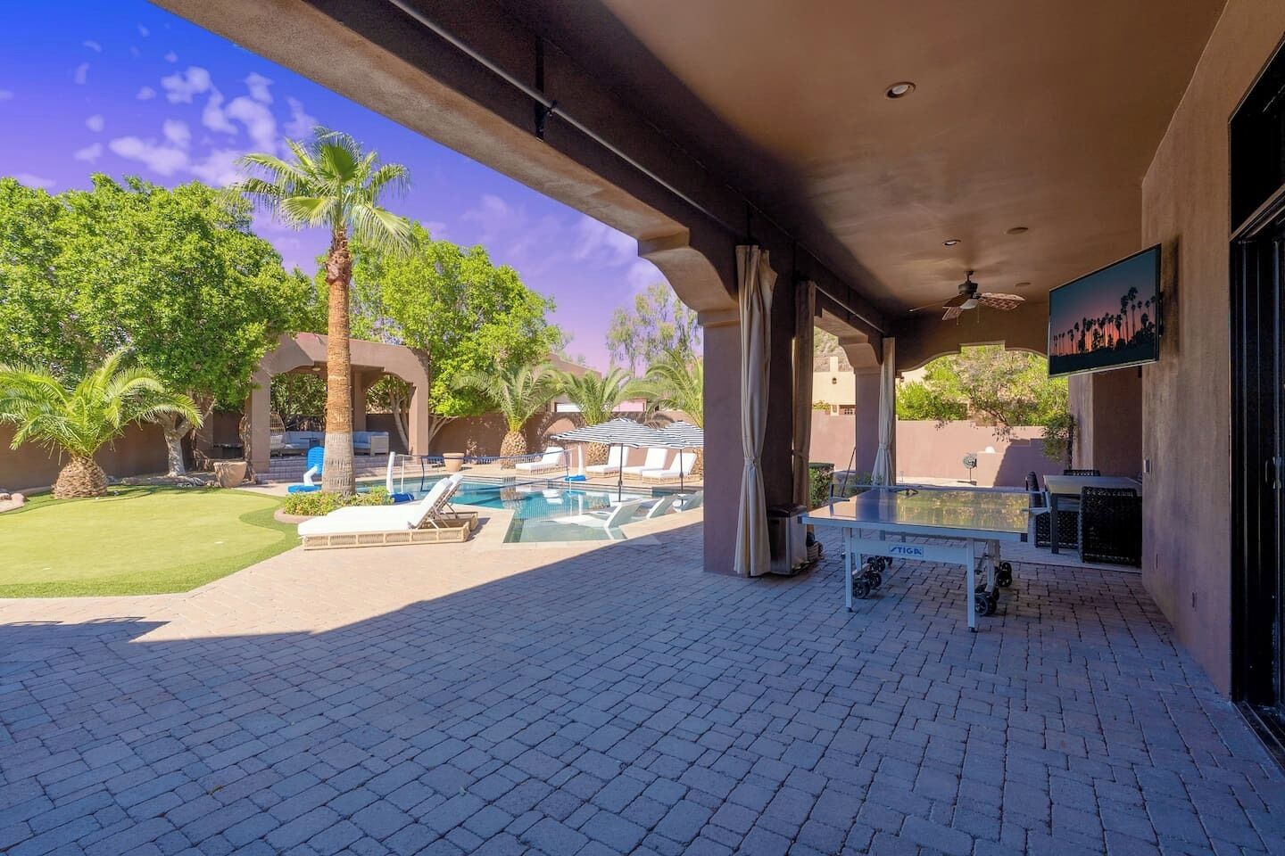A covered outdoor area with a pool, lounge chairs, and a table.