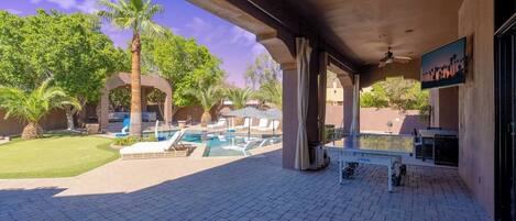 A covered outdoor area with a pool, lounge chairs, and a table.