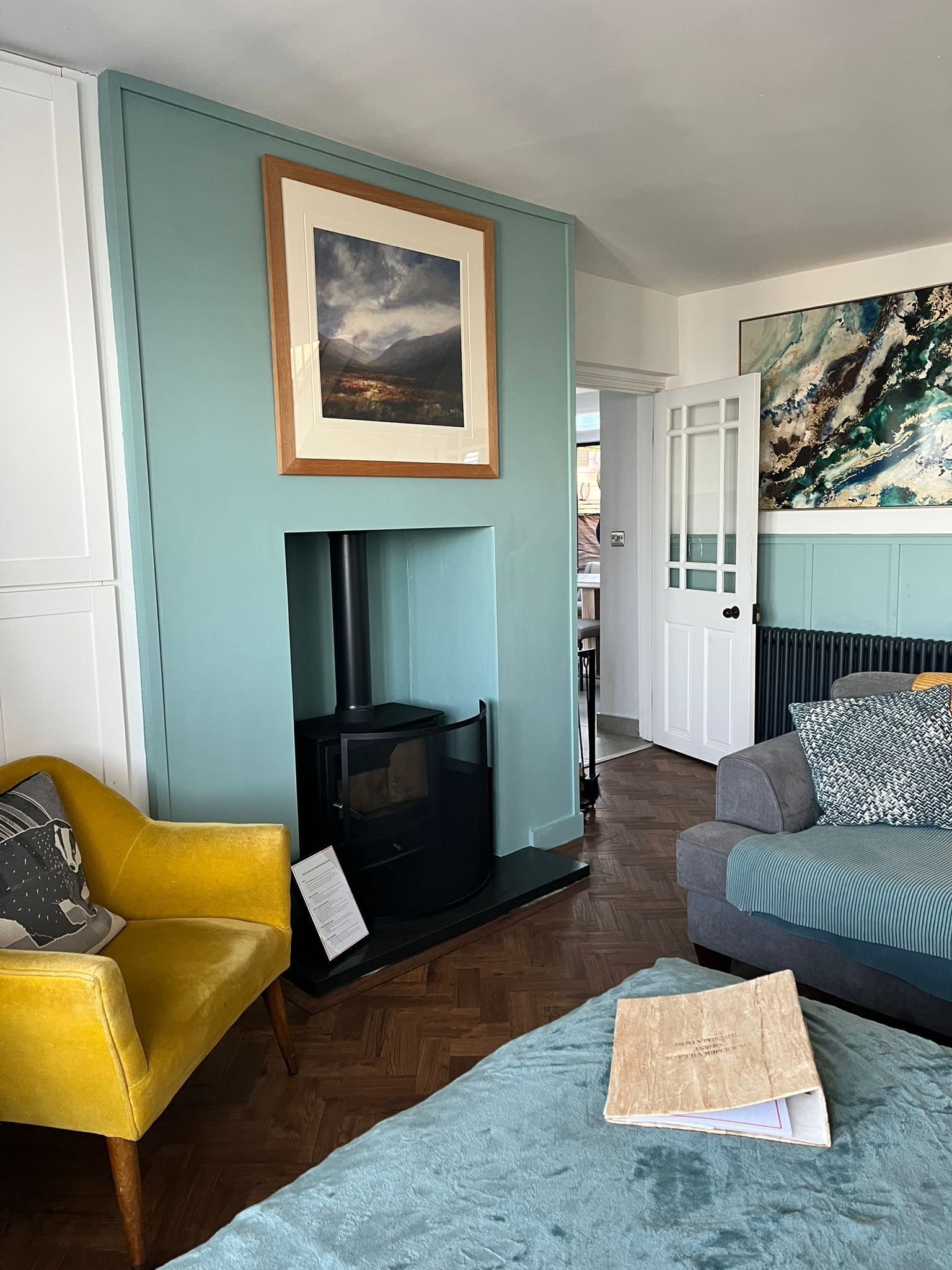 A living room with a fireplace, a yellow armchair, a grey sofa, and a blue armchair.