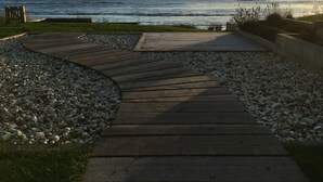 Un sendero de madera que lleva a una playa de piedras y césped.