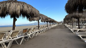 A beach with rows of sun loungers and thatched umbrellas.