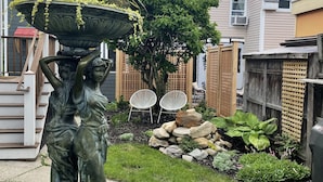 Un jardin agrémenté d’une statue, d’un grand bac à fleurs et d’un arbre.
