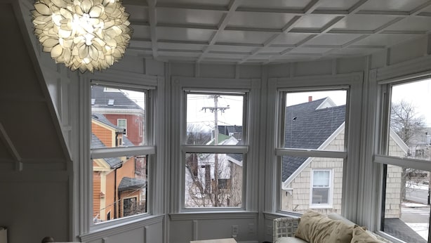 Une chambre avec un grand lit, une table de chevet en bois, un canapé blanc orné de coussins à motifs et une grande fenêtre à carreaux.
