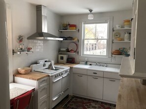 A compact kitchen with white cabinets, a stove, a sink, and a window overlooking a backyard.