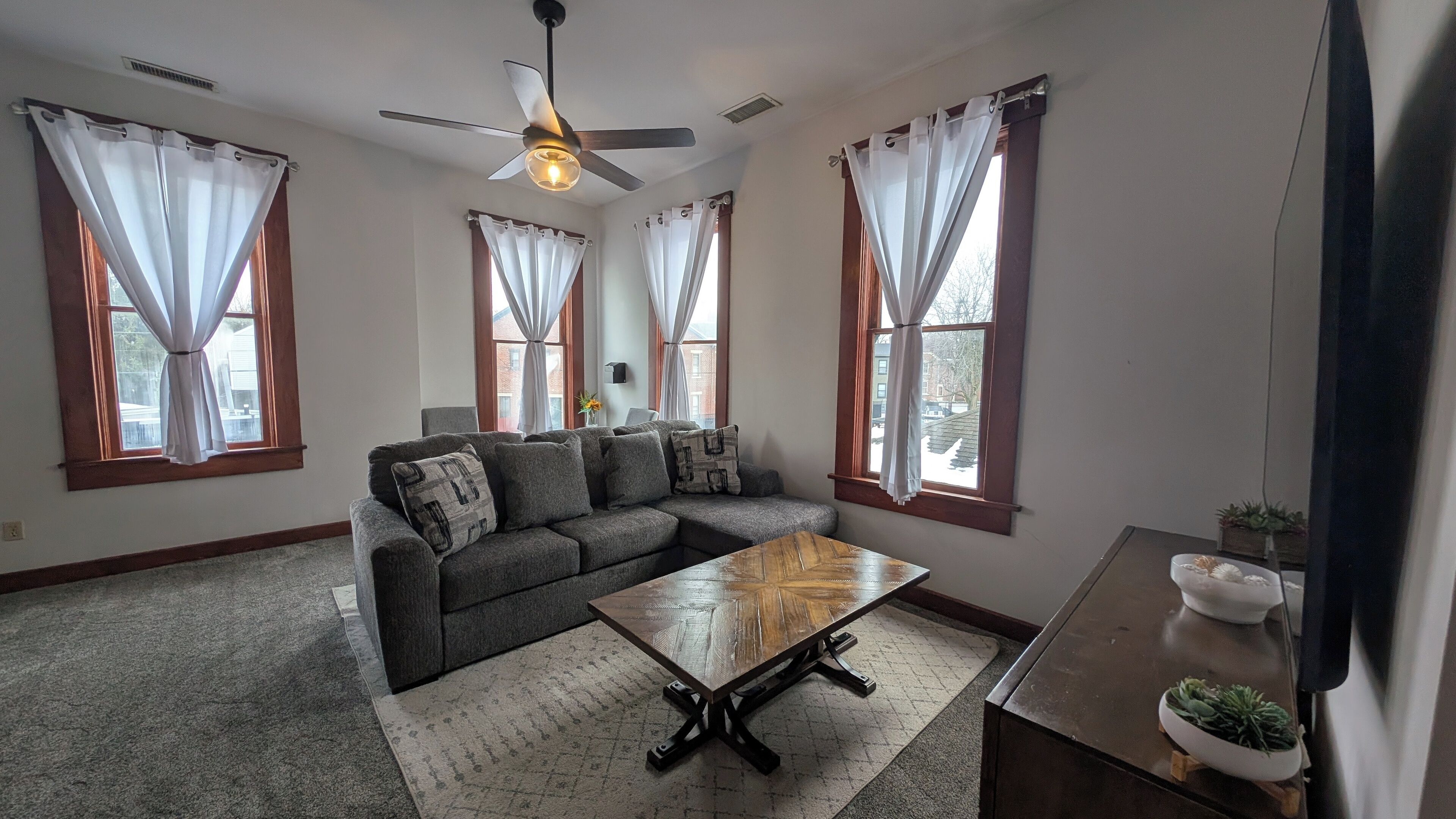 A living room with a sectional sofa, a wooden coffee table, and a ceiling fan.