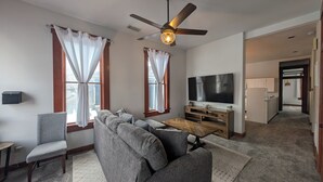 Un salon avec un canapé gris, une table basse en bois, un téléviseur à écran plat et un ventilateur de plafond.