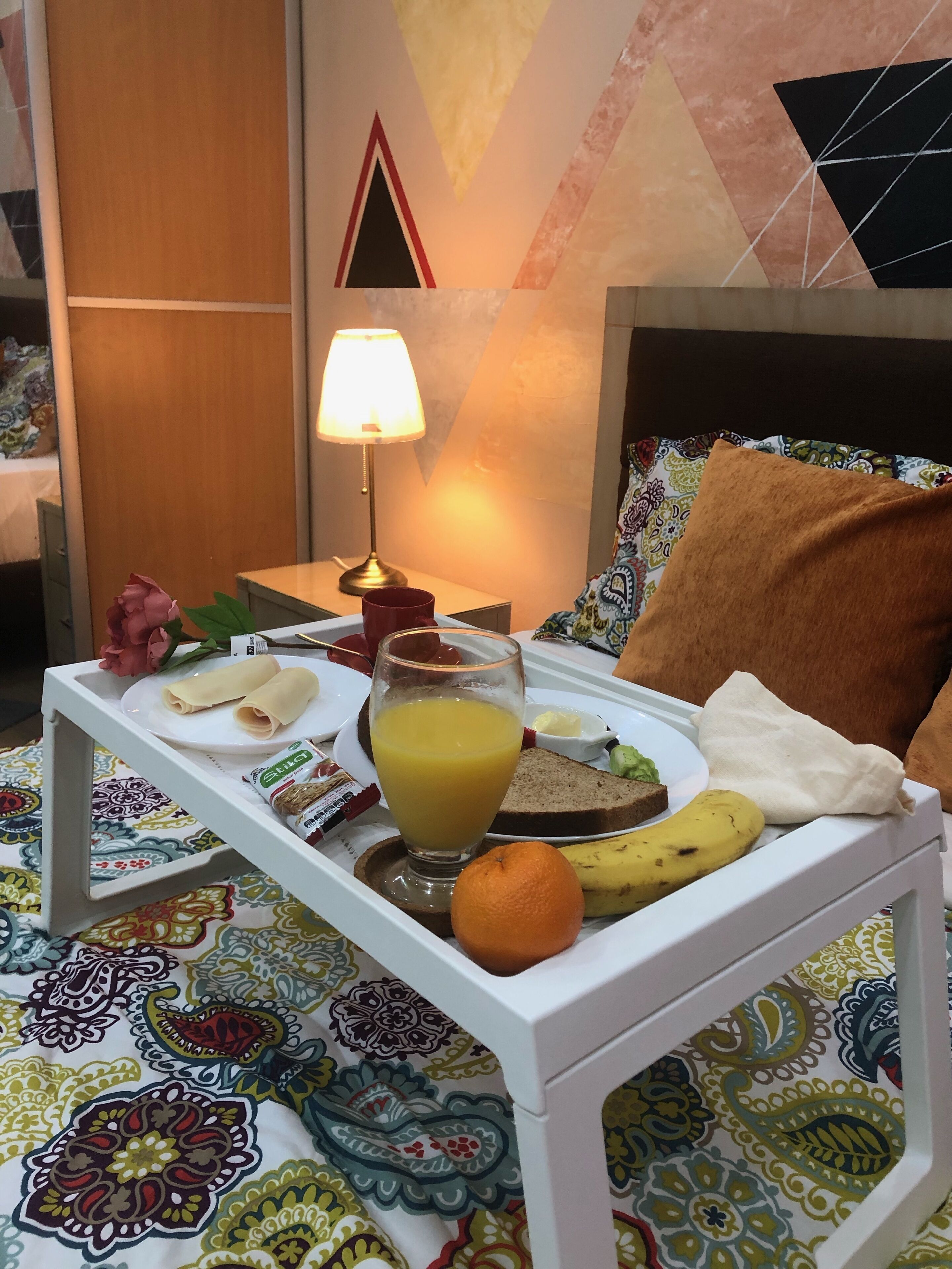 A breakfast tray with a glass of orange juice, a banana, an orange, and a plate with bread and a small bowl of butter.