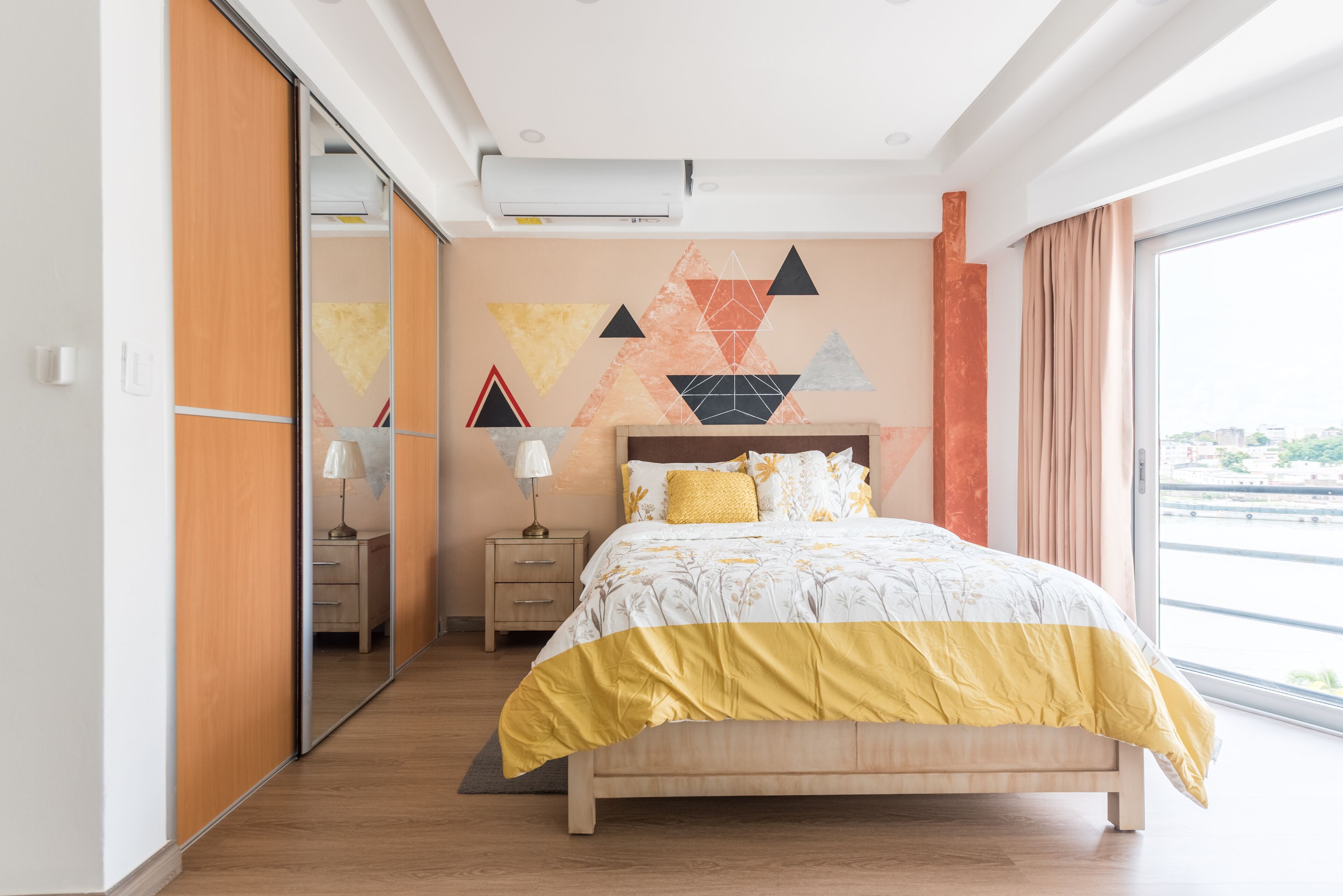 Un dormitorio moderno con una cama, una mesita de noche, un espejo y un diseño geométrico en la pared.