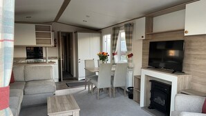 A modern living room with a sofa, coffee table, TV, fireplace, and dining area. - Arum dog friendly caravan on Rockley Park, Poole (Poole)