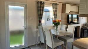 A compact kitchen with a dining area, a sliding glass door, and a small TV. - Arum dog friendly caravan on Rockley Park, Poole (Poole)