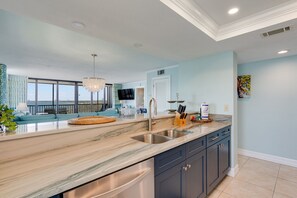 A modern kitchen with a marble countertop, stainless steel sink, and dark cabinetry.