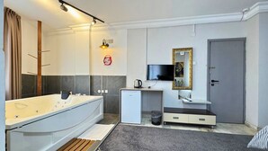 A modern bathroom with a bathtub, a small desk with a kettle, a television, and a door. - Grond Konaklama Mersin (Mersin)