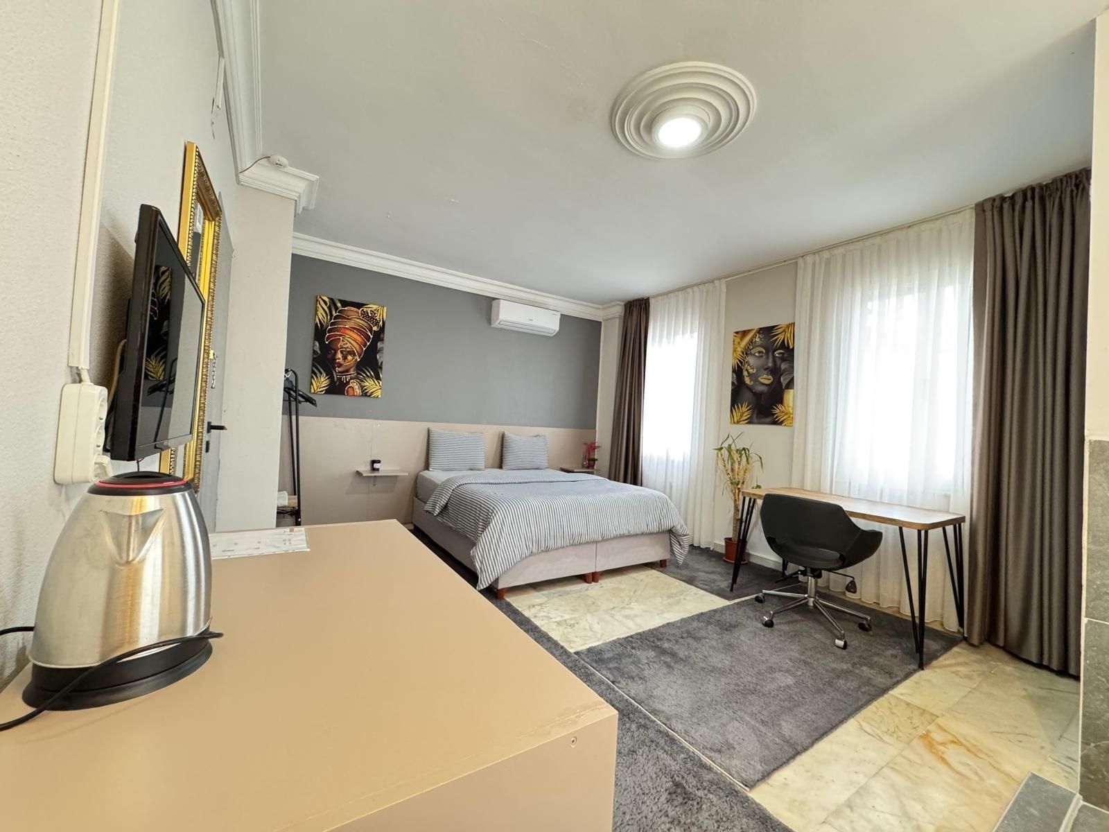 A hotel room with a bed, a desk, a chair, a TV, and artwork on the walls.