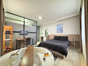 A modern hotel room with a large bed, a wooden chair, a desk, a TV, a painting, and a bathtub with toiletries. - Grond Konaklama Mersin (Mersin)