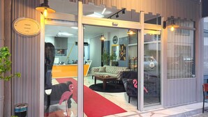 A modern interior with a reception desk, a sofa, a red carpet, and a glass door. - Grond Konaklama Mersin (Mersin)