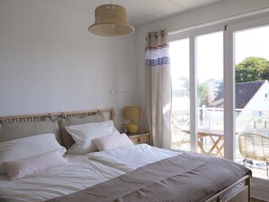 Ein Schlafzimmer mit Bett, Nachttischlampe, einem Fenster mit Vorhängen und Blick auf Gebäude.