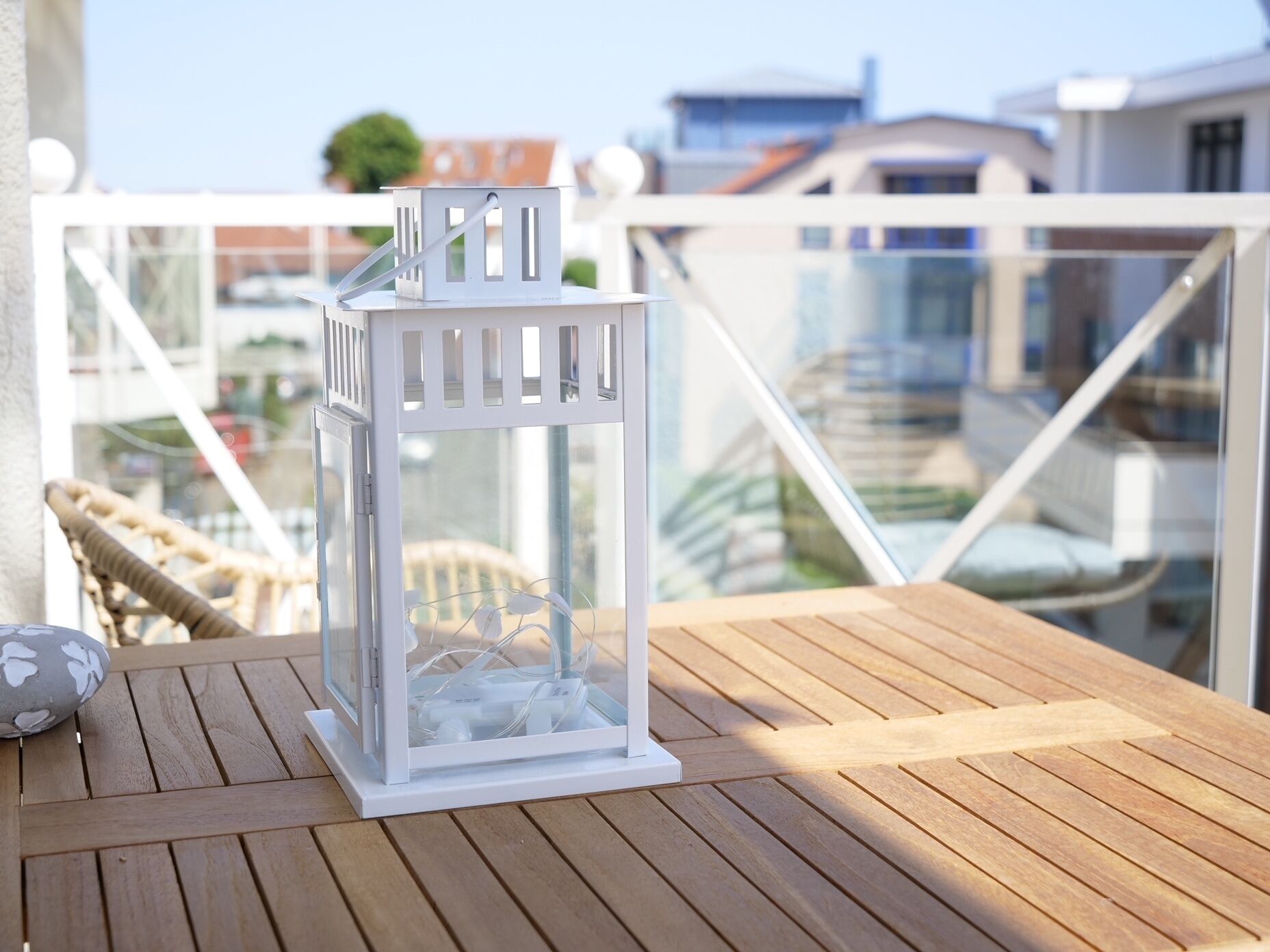 A white lantern on a wooden table on a balcony with a view of buildings.