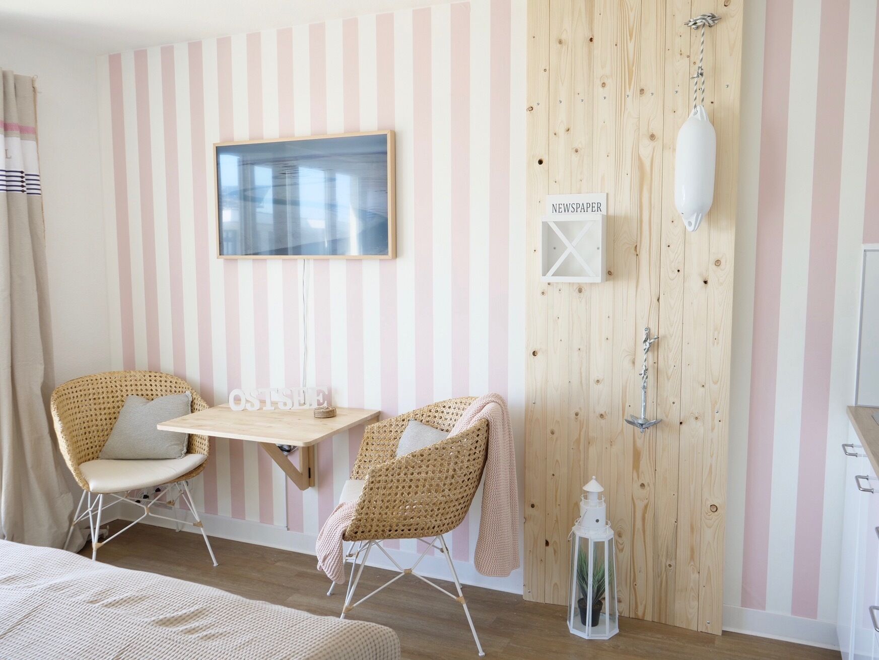 A room with striped wallpaper, a wooden door, a table with chairs, a hanging lamp, and a framed picture on the wall.