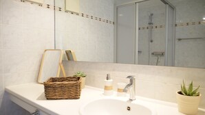 A bathroom with a white sink, a mirror, a shower, and a wicker basket with a plant.