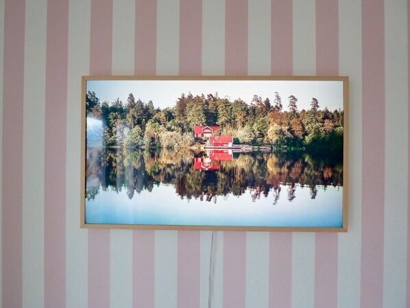 Ein gerahmtes Foto von einem stillen See, mit einem roten Haus und dichten Bäumen, die sich im Wasser spiegeln.