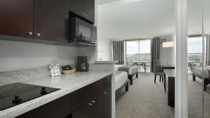 A modern hotel room with a kitchen area, a bed, a desk, and a view of the city. - Soothing urban retreat with stunning views of the Koolau Mountains. (Honolulu)