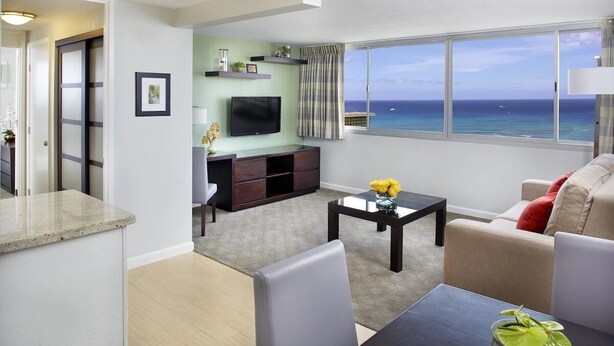 A modern living room with a large window, a flat-screen TV, and a dining area. - Soothing urban retreat with stunning views of the Koolau Mountains. (Honolulu)