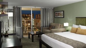 A hotel room with a bed, a sofa, a desk, and a view of the city at night. - Soothing urban retreat with stunning views of the Koolau Mountains. (Honolulu)
