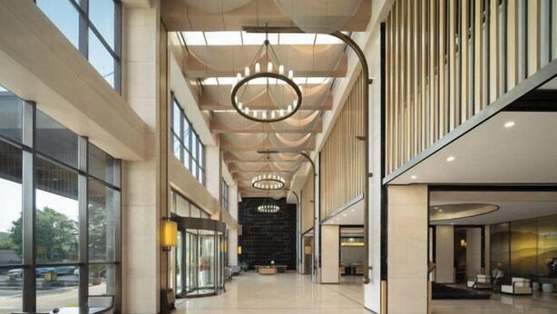 Un vestíbulo amplio con techos altos, ventanas grandes y candelabros modernos.
