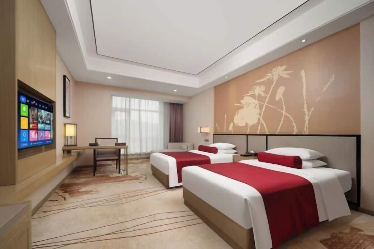 Habitación de hotel con dos camas, un escritorio, un televisor y un gran mural floral.