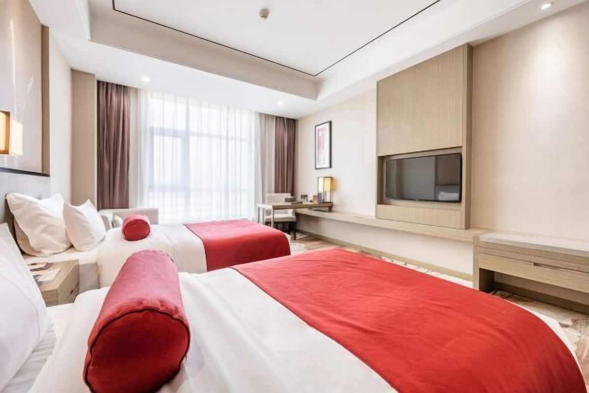 Habitación de hotel con dos camas, un escritorio, un televisor y un ventanal grande.