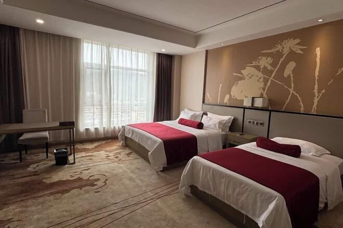 Una habitación de hotel con dos camas, un escritorio y un ventanal con cortinas.