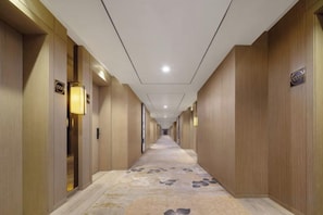 Un pasillo de hotel con puertas a ambos lados, iluminación en el techo y una alfombra estampada.